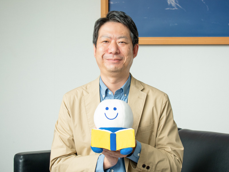 よむよむ君人形を持ってほほ笑む千田竜也さん